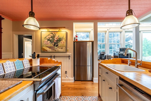 kitchen with stainless steel appliances, sink, white cabinets, and decorative light fixtures