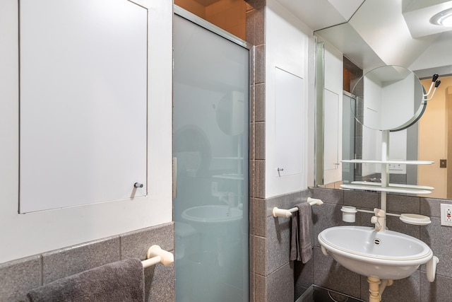 bathroom featuring a shower with door, sink, and tile walls