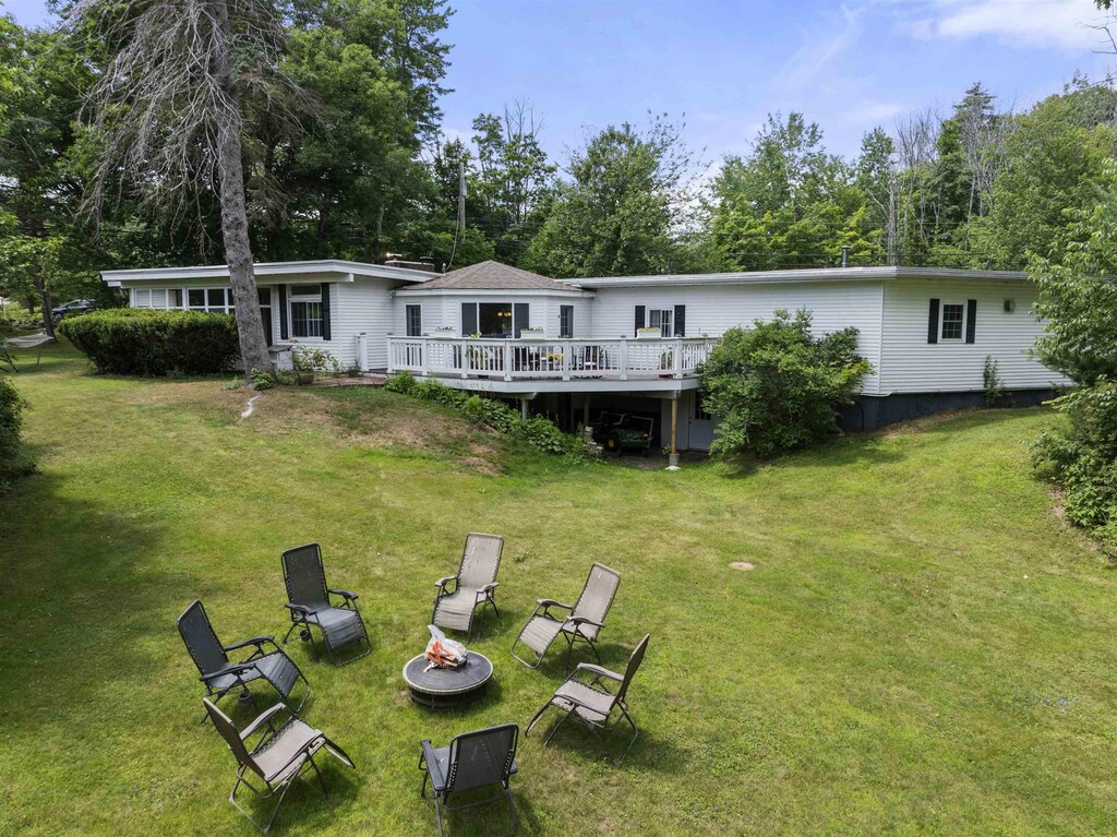 back of property featuring a lawn, a deck, and an outdoor fire pit