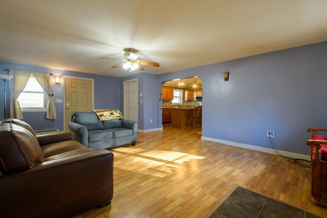 living room featuring baseboard heating, ceiling fan, and light wood-type flooring