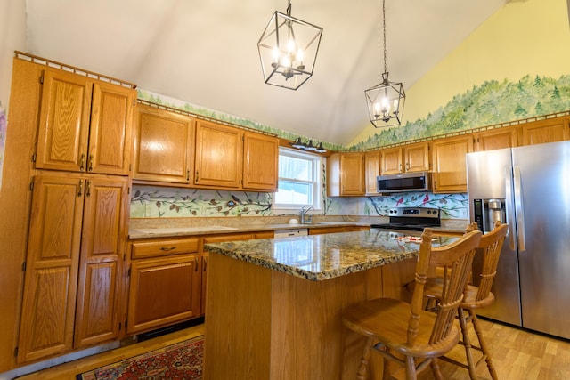 kitchen featuring decorative light fixtures, a center island, vaulted ceiling, stainless steel appliances, and light hardwood / wood-style floors