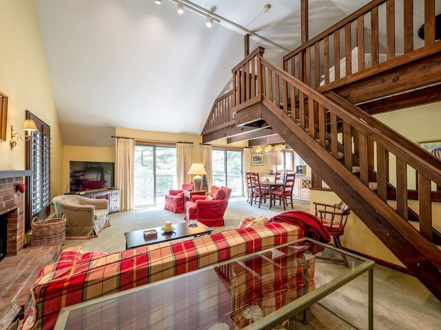 carpeted living room with a notable chandelier, high vaulted ceiling, track lighting, and a brick fireplace