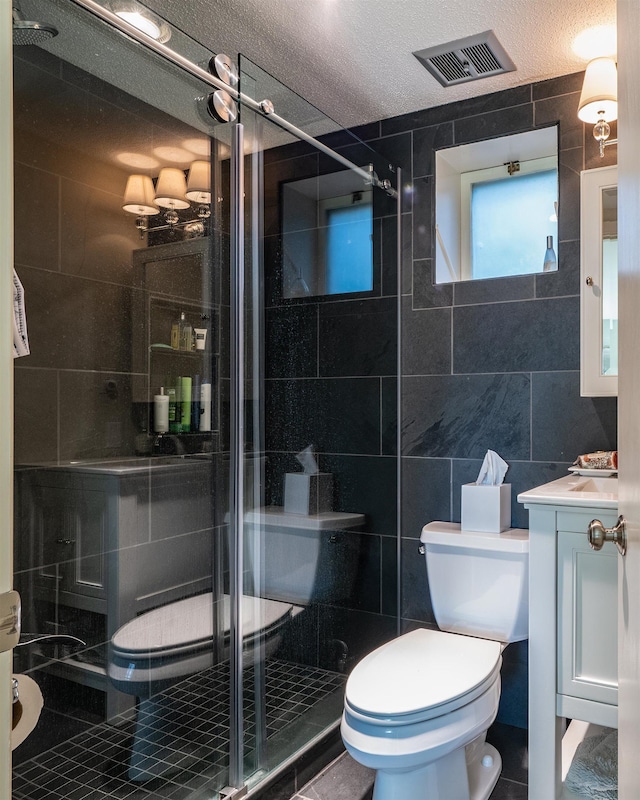 bathroom featuring a textured ceiling, toilet, vanity, a shower with shower door, and tile walls