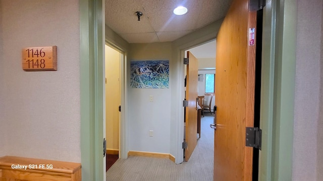 hall with light colored carpet and a drop ceiling