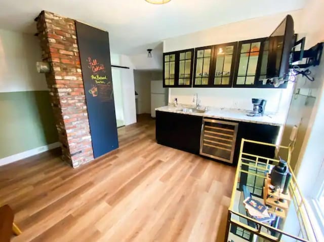 kitchen featuring light hardwood / wood-style flooring, refrigerator, beverage cooler, brick wall, and sink