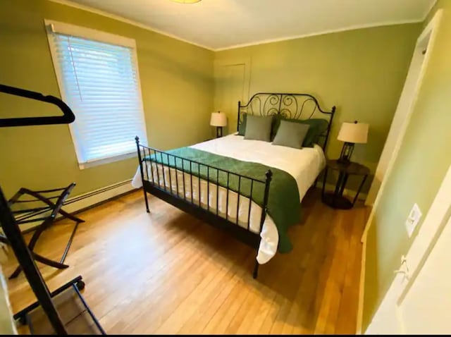 bedroom featuring crown molding, a baseboard heating unit, and hardwood / wood-style floors