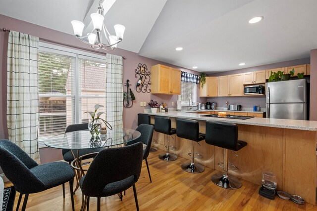 kitchen with light wood-type flooring, stainless steel appliances, light brown cabinetry, kitchen peninsula, and hanging light fixtures