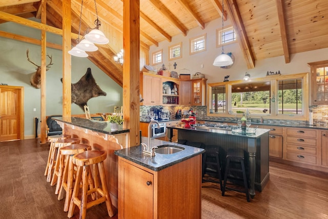 kitchen featuring pendant lighting, dark stone counters, a breakfast bar, and a kitchen island with sink