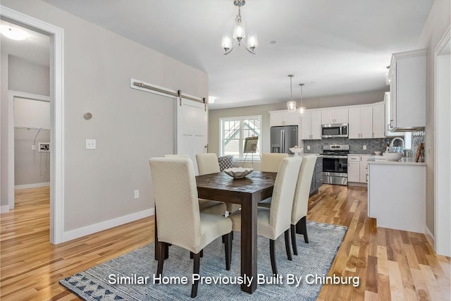 dining area featuring a barn door, sink, a chandelier, and light hardwood / wood-style flooring