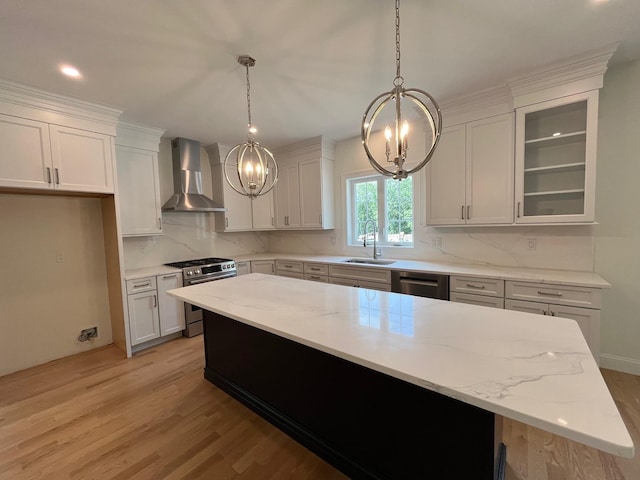 kitchen with stainless steel appliances, a sink, a kitchen island, light wood-type flooring, and wall chimney exhaust hood