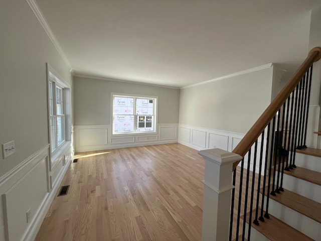 unfurnished room featuring light wood-style flooring, a decorative wall, visible vents, stairs, and ornamental molding