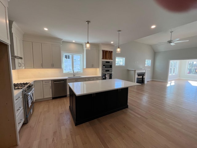 kitchen featuring light wood-style flooring, a kitchen island, a sink, light countertops, and appliances with stainless steel finishes