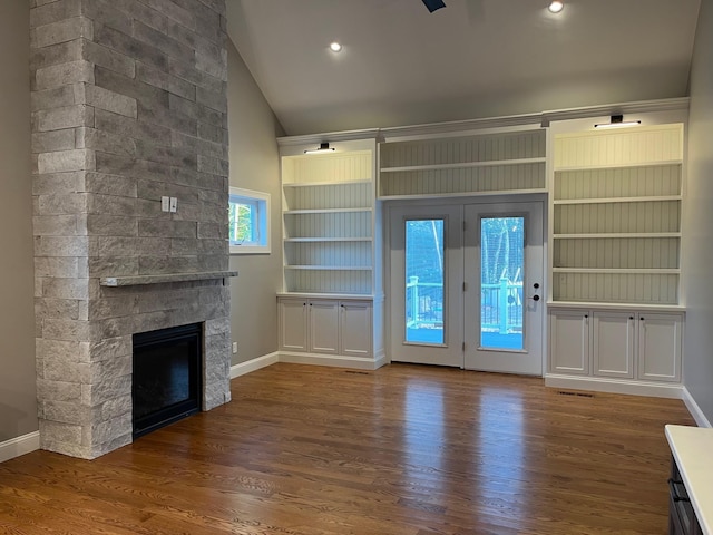 unfurnished living room with baseboards, vaulted ceiling, wood finished floors, and a stone fireplace