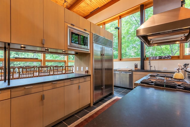 kitchen with wood ceiling, island exhaust hood, dark tile patterned flooring, built in appliances, and sink