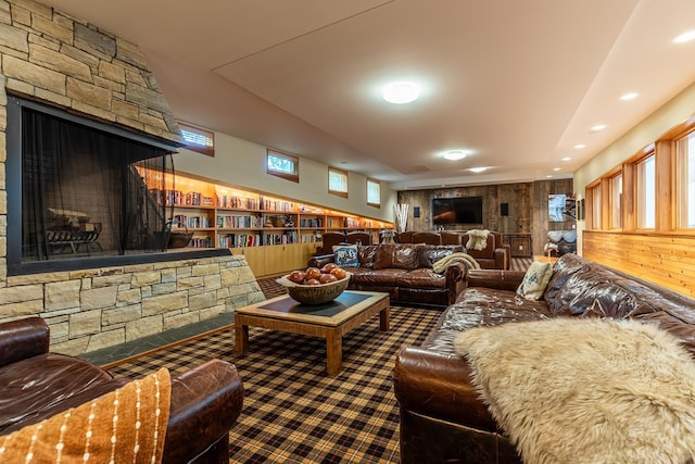 living room with built in shelves, a stone fireplace, and wooden walls