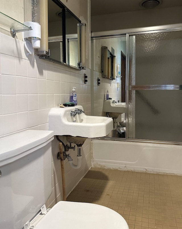 full bathroom with combined bath / shower with glass door, sink, toilet, tile walls, and tasteful backsplash