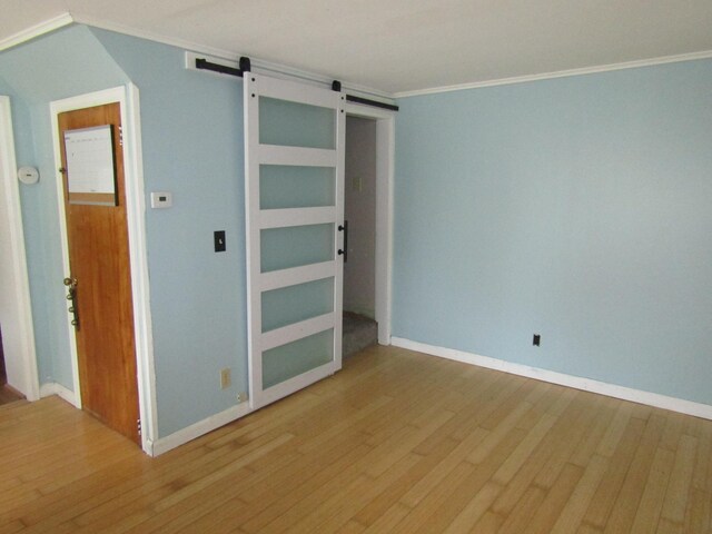 unfurnished bedroom featuring ornamental molding, hardwood / wood-style flooring, and a barn door