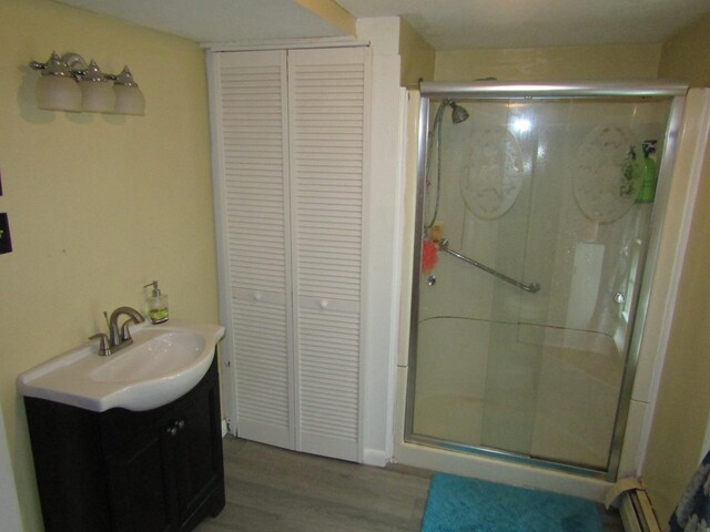 bathroom with hardwood / wood-style flooring, a baseboard heating unit, an enclosed shower, and vanity