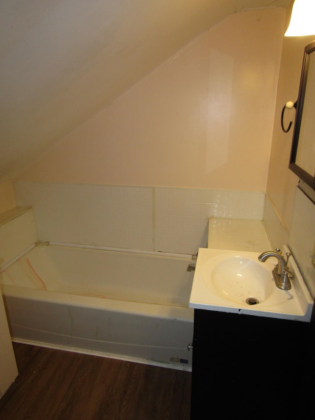 bathroom with vanity, vaulted ceiling, hardwood / wood-style floors, and a tub to relax in