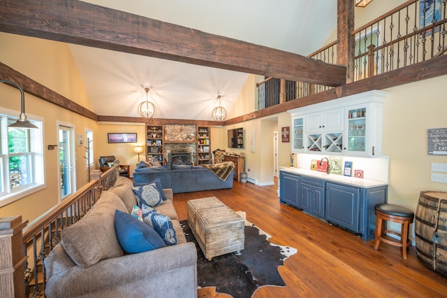 living room with beam ceiling, indoor bar, a fireplace, hardwood / wood-style floors, and a high ceiling