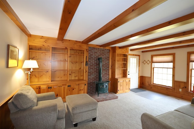 carpeted living room with wood walls, brick wall, beamed ceiling, and a wood stove