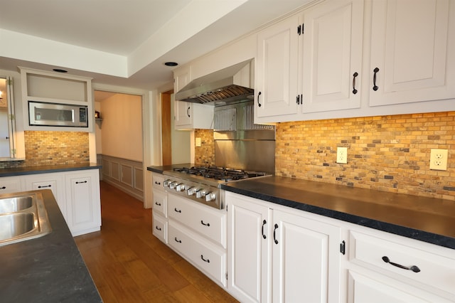 kitchen with appliances with stainless steel finishes, white cabinets, wall chimney range hood, backsplash, and dark wood-type flooring