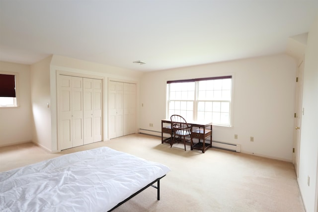 bedroom featuring light carpet, a baseboard radiator, and two closets