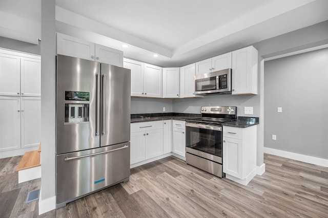 kitchen featuring dark stone countertops, light hardwood / wood-style flooring, white cabinets, and appliances with stainless steel finishes