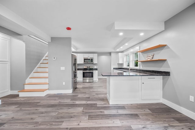 kitchen featuring dark stone countertops, kitchen peninsula, hardwood / wood-style flooring, stainless steel appliances, and white cabinets