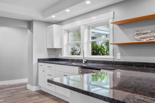 kitchen with sink, dark stone counters, white cabinets, and light wood-type flooring