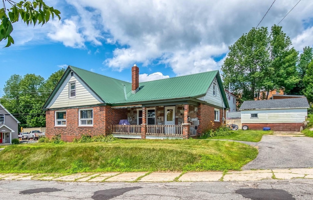 view of front of property with a front yard, covered porch, a chimney, brick siding, and metal roof