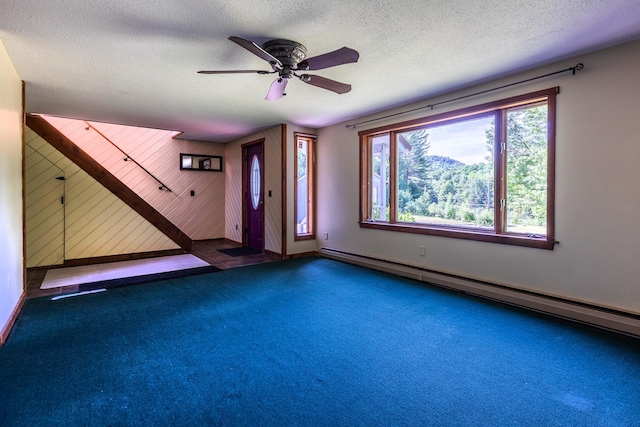 interior space featuring wooden walls, ceiling fan, a baseboard heating unit, and a textured ceiling