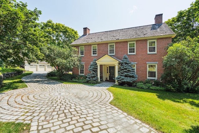 colonial home with a high end roof, a chimney, a front lawn, and brick siding