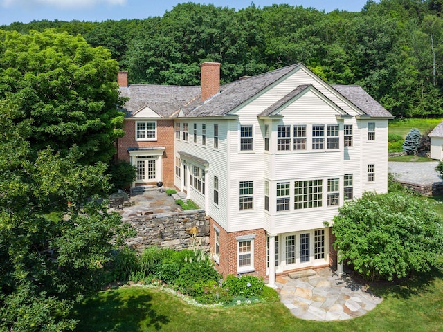 back of property with a chimney, french doors, a patio area, a wooded view, and brick siding