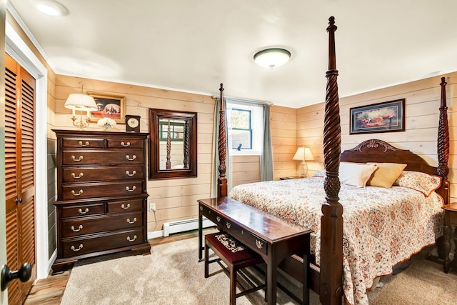 bedroom with a baseboard heating unit, wooden walls, light colored carpet, and a closet