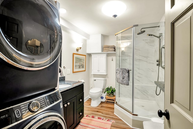 bathroom with stacked washer and dryer, vanity, wood-type flooring, a shower with shower door, and toilet