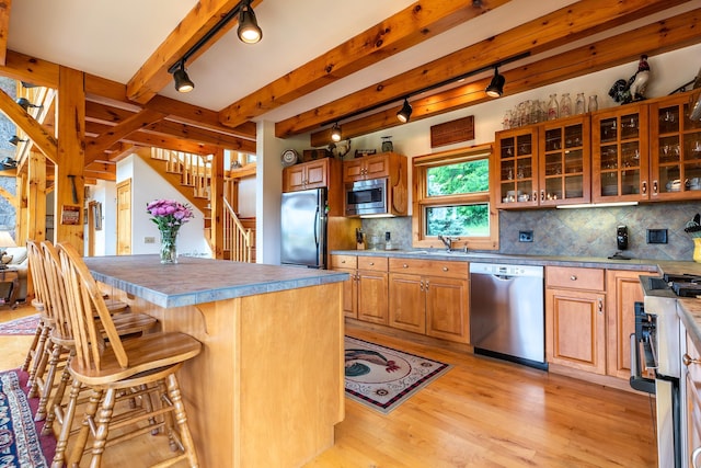 kitchen featuring appliances with stainless steel finishes, backsplash, a kitchen bar, a center island, and light hardwood / wood-style flooring