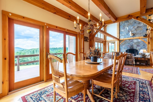 dining room featuring a stone fireplace, an inviting chandelier, a mountain view, beam ceiling, and light hardwood / wood-style flooring