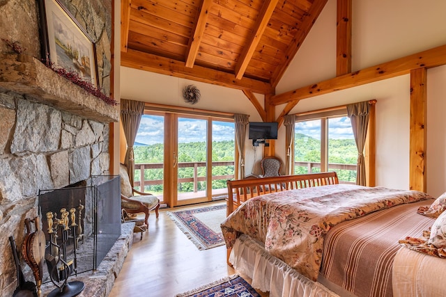 bedroom with access to exterior, beam ceiling, hardwood / wood-style floors, a stone fireplace, and wooden ceiling