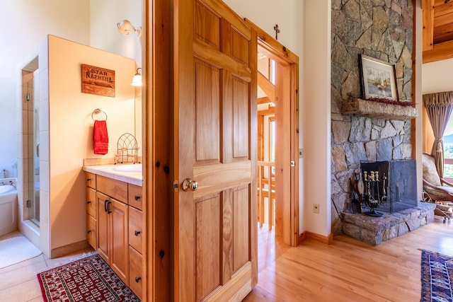 bathroom with vanity, hardwood / wood-style floors, a stone fireplace, and a shower with shower door