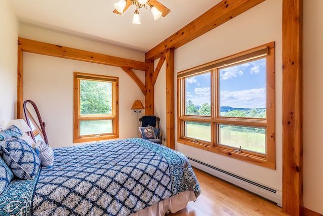 bedroom featuring baseboard heating, beam ceiling, a mountain view, and light wood-type flooring