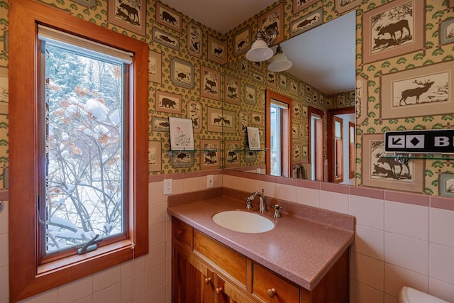 half bathroom featuring wainscoting, vanity, wallpapered walls, and tile walls