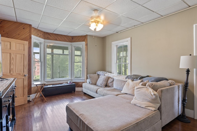 living room with plenty of natural light, dark wood-type flooring, a paneled ceiling, and wooden walls