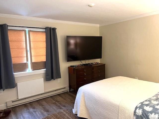 bedroom with dark hardwood / wood-style floors, baseboard heating, and crown molding