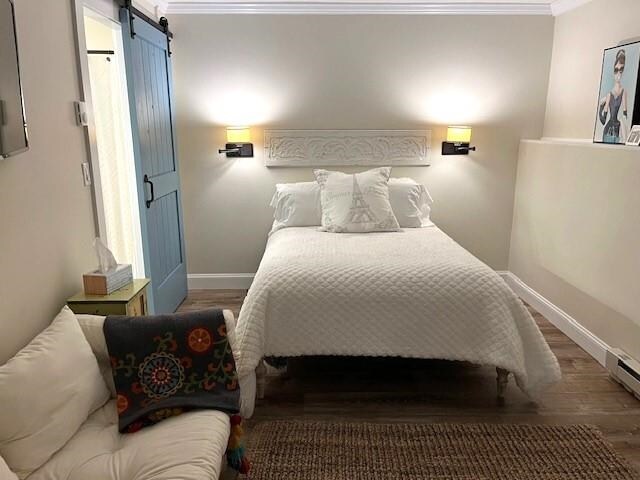 bedroom with ornamental molding, a barn door, and hardwood / wood-style floors