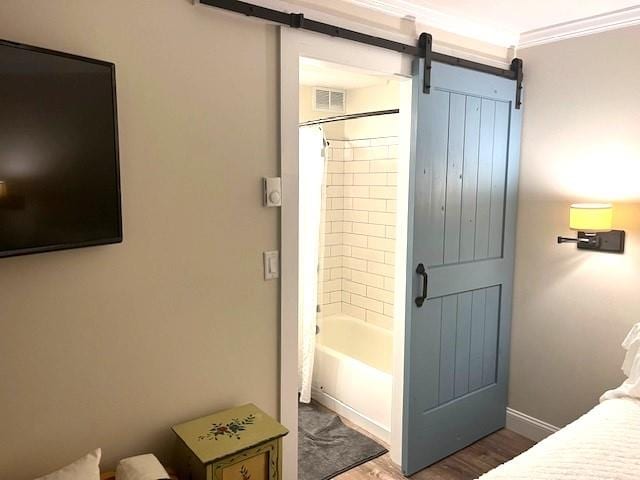 bedroom featuring crown molding, hardwood / wood-style floors, and a barn door