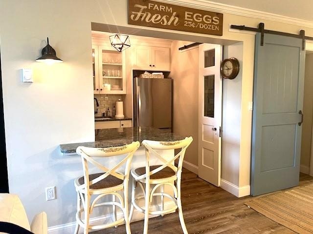 kitchen with stainless steel refrigerator, a barn door, decorative backsplash, hardwood / wood-style flooring, and ornamental molding