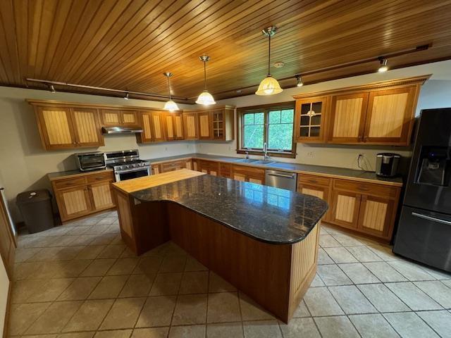 kitchen featuring light tile patterned floors, under cabinet range hood, stainless steel appliances, a sink, and brown cabinets