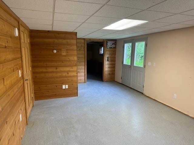 empty room with a paneled ceiling, wood walls, and concrete floors