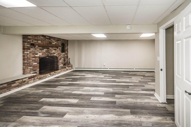 basement with a baseboard radiator, brick wall, dark hardwood / wood-style floors, and a paneled ceiling